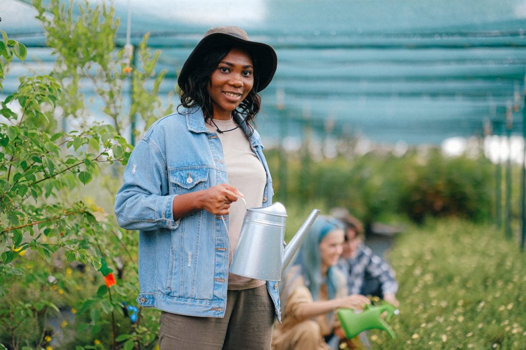 Home A cheerful woman holding a watering can in a greenhouse, tending to plants.